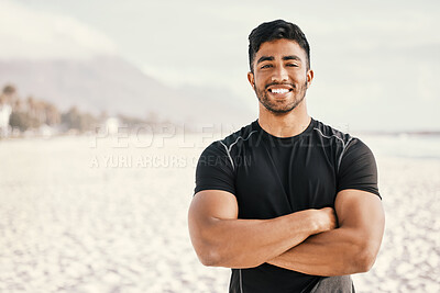 Buy stock photo Shot of a sporty young man standing with his arms crossed while out for a workout at the beach