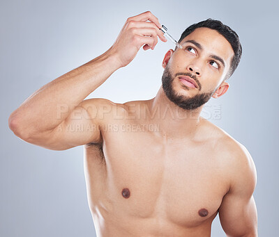 Buy stock photo Studio shot of a handsome young man applying serum to his face against a grey background