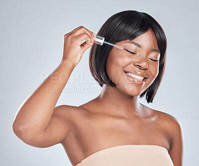 Buy stock photo Studio shot of an attractive young woman applying serum to her face against a grey background