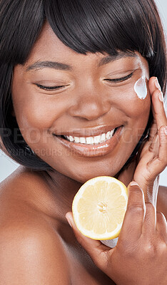 Buy stock photo Studio shot of an attractive young woman holding a lemon and applying moisturiser to her face against a grey background