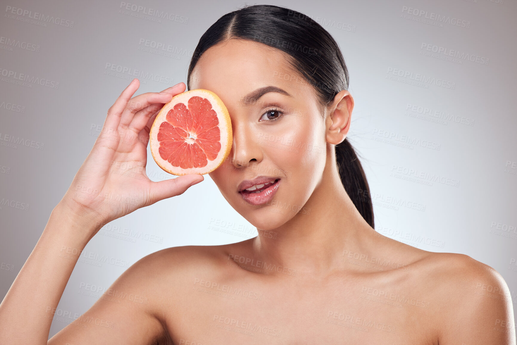 Buy stock photo Studio portrait of a beautiful young woman posing with grapefruit against a grey background