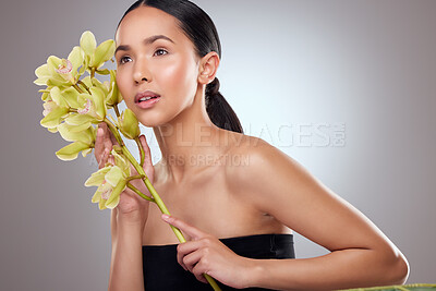 Buy stock photo Studio shot of a beautiful young woman posing with orchids against a grey background