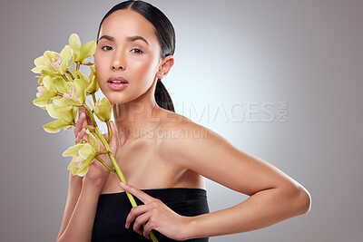 Buy stock photo Studio portrait of a beautiful young woman posing with orchids against a grey background