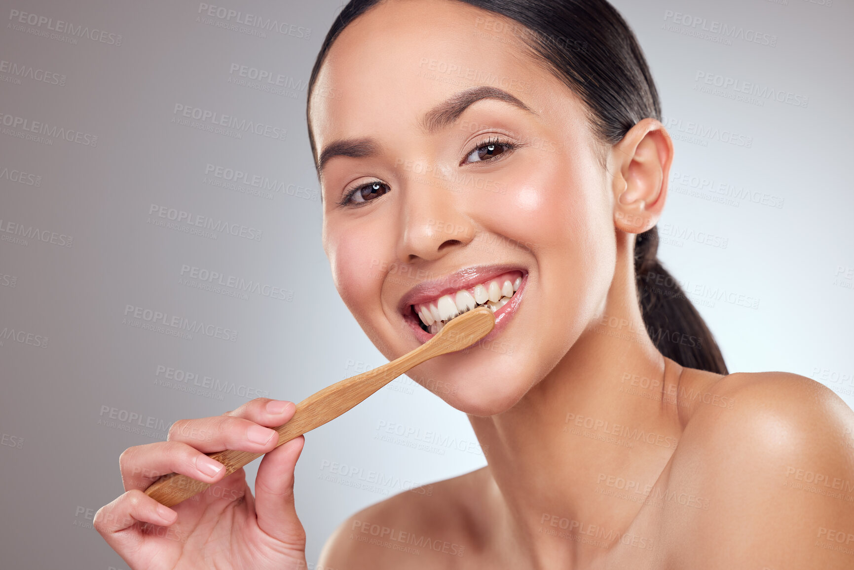 Buy stock photo Studio portrait of a beautiful young woman brushing her teeth against a grey background
