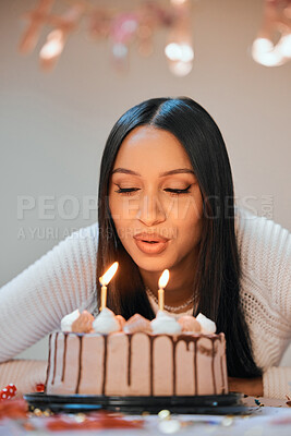 Buy stock photo Shot of a young woman blowing candles on a cake while celebrating her birthday at home