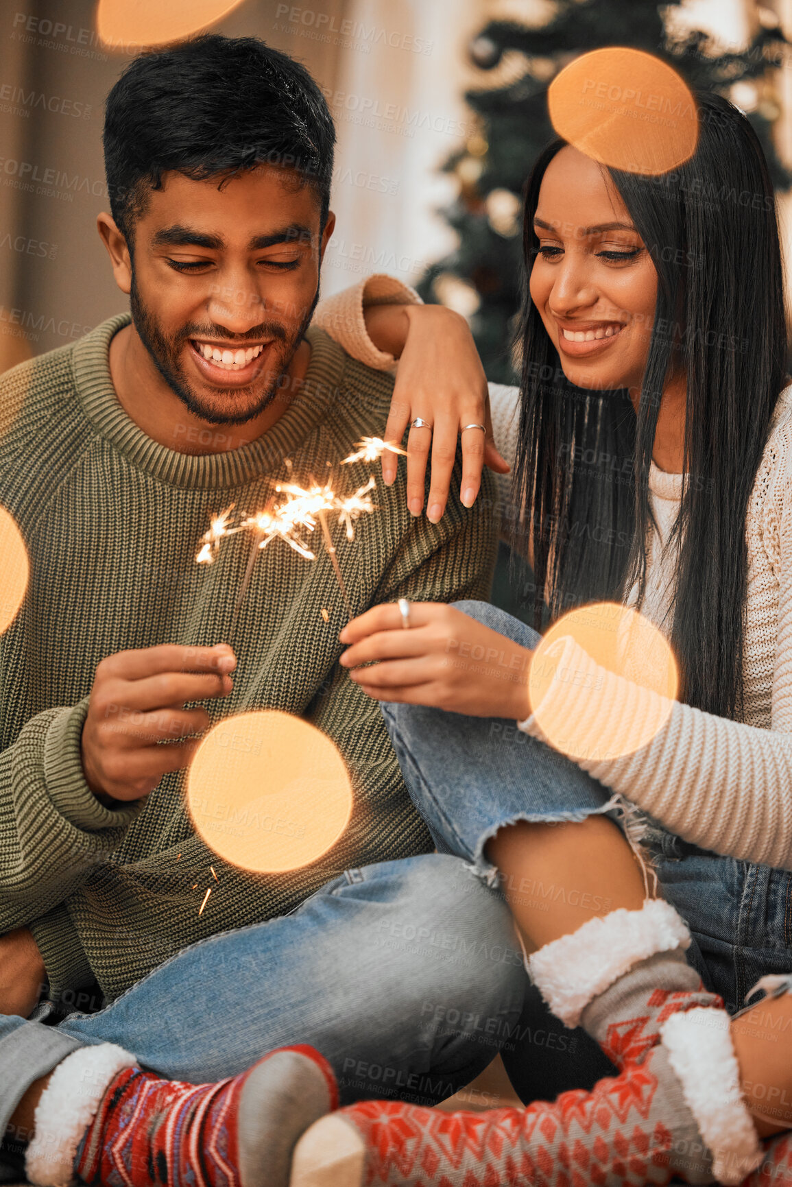 Buy stock photo Shot of a young couple holding sparklers while celebrating Christmas together at home