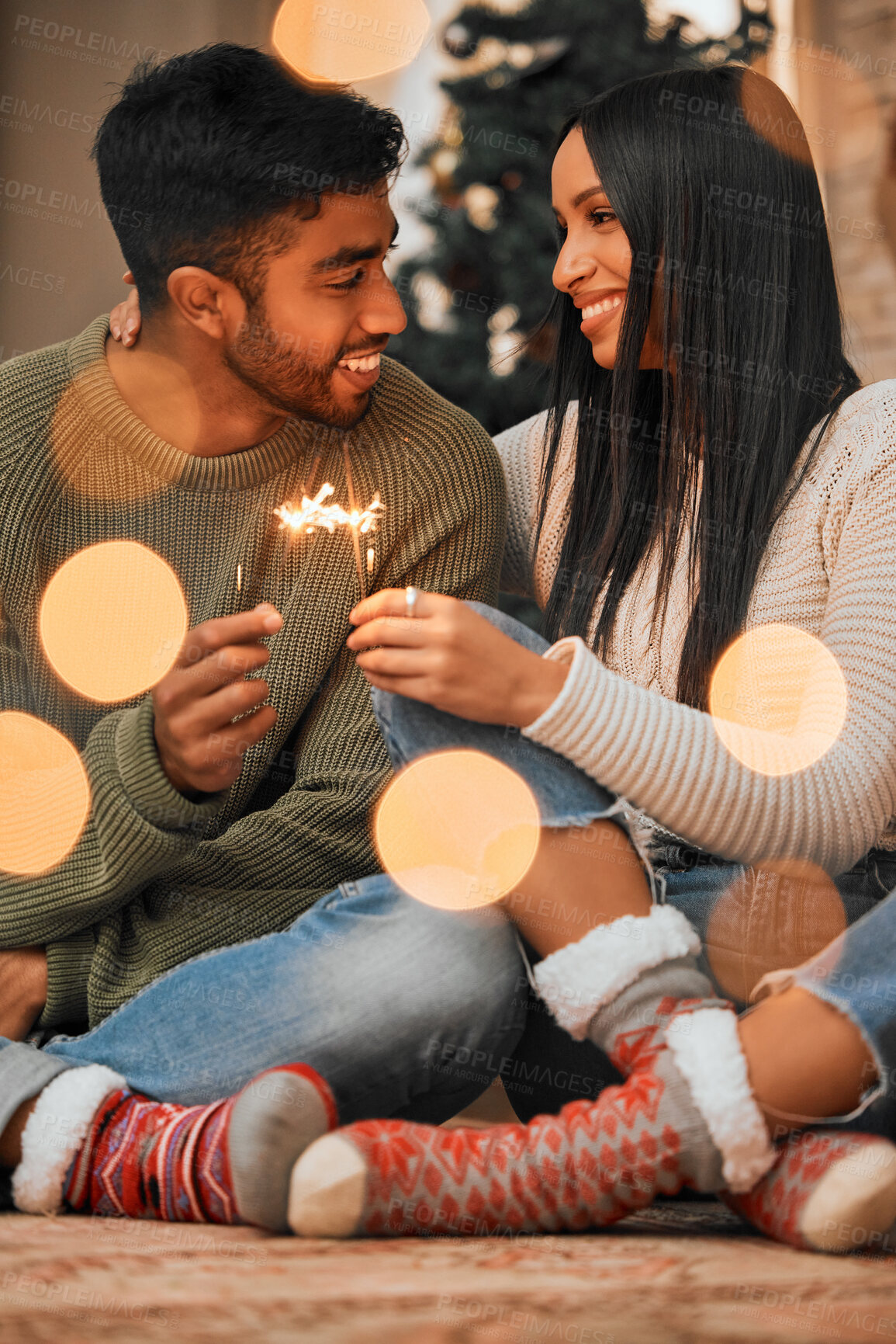 Buy stock photo Shot of a young couple holding sparklers while celebrating Christmas together at home
