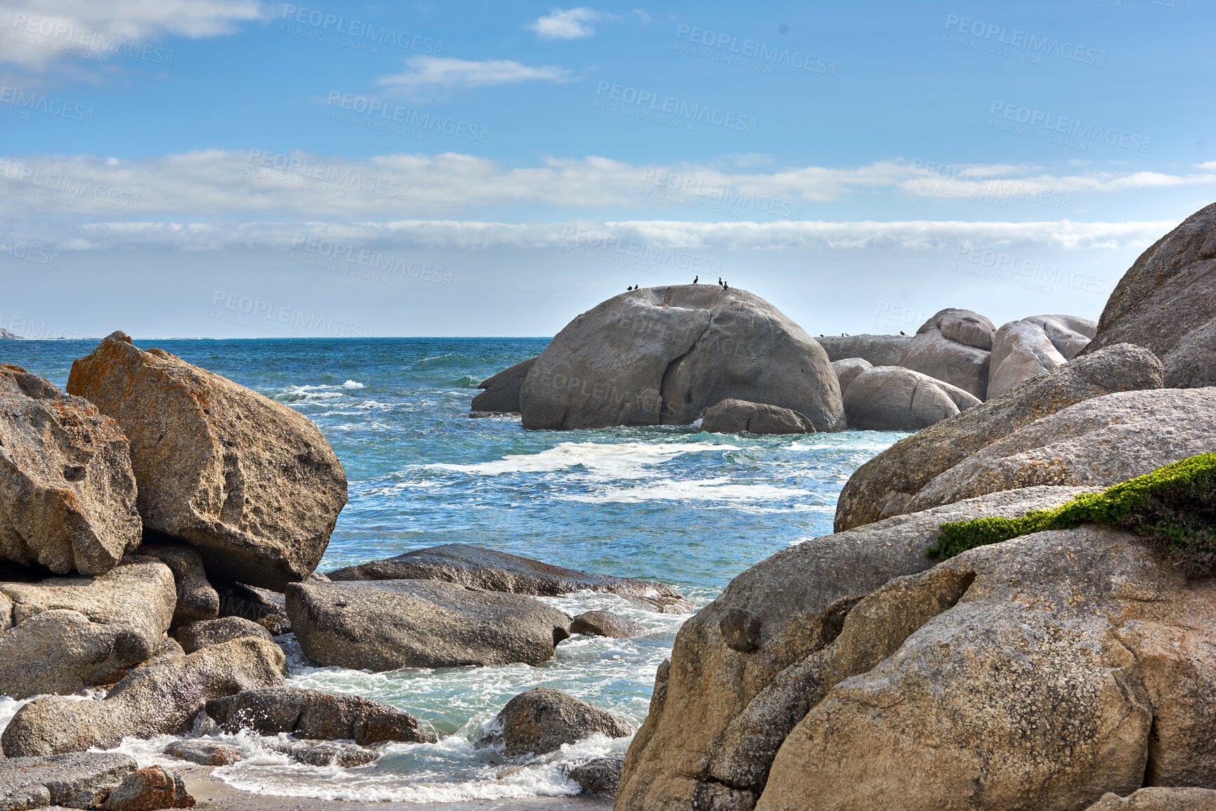 Buy stock photo Beautiful sea view of big boulders and ocean water on a sunny beach day in summer. A seaside view of nature with a blue sky, white clouds, and waves. A seascape near the shore under the horizon