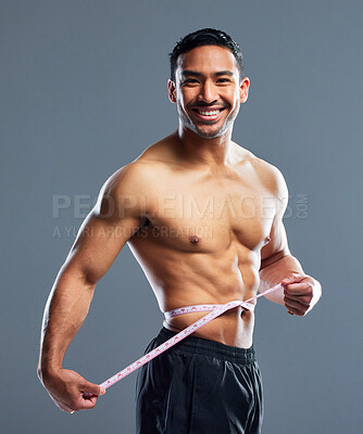 Buy stock photo Studio portrait of a muscular young man measuring his waist against a grey background