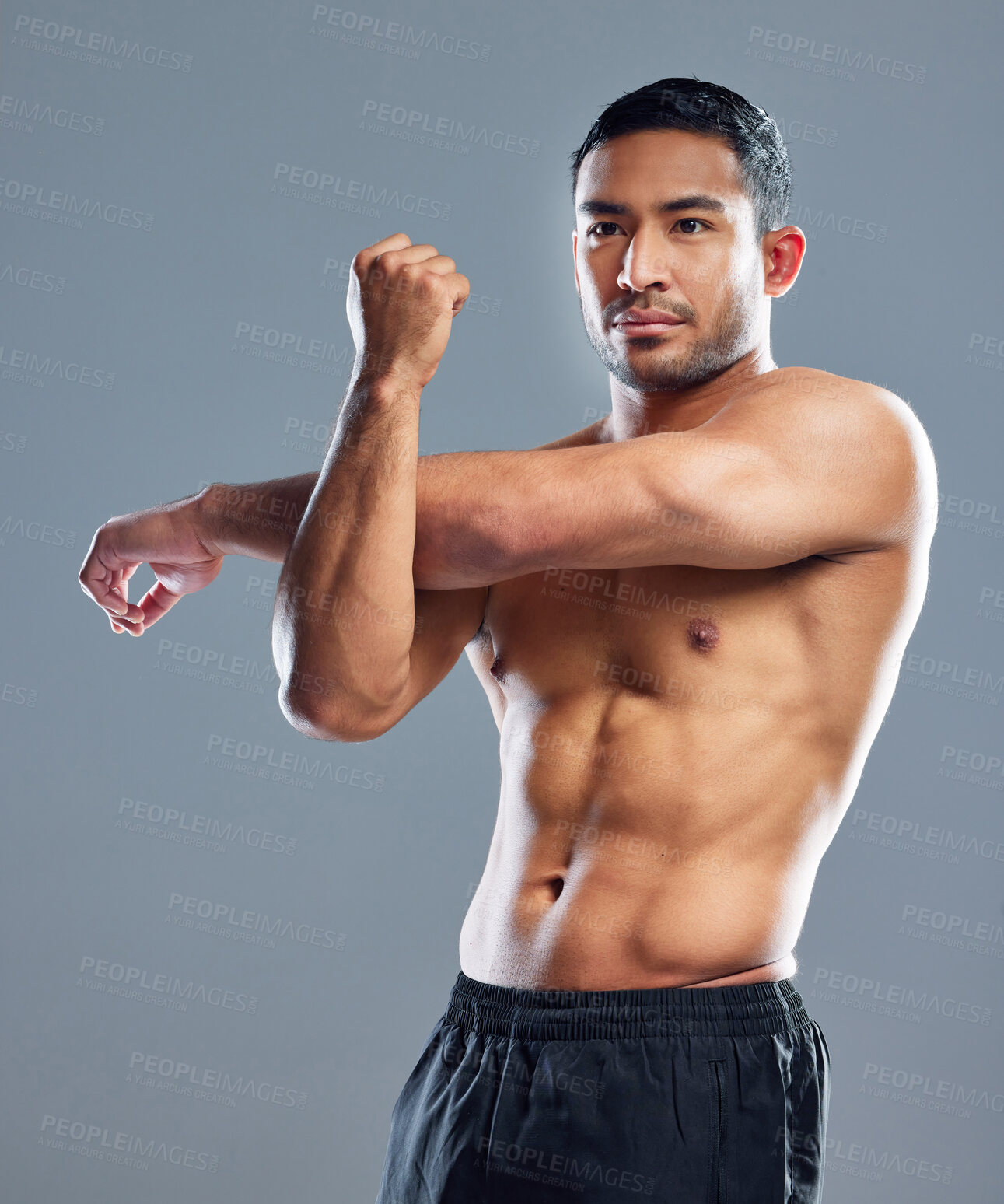 Buy stock photo Studio shot of a muscular young man stretching his arms against a grey background