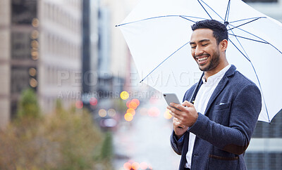 Buy stock photo Cropped shot of a handsome young businessman sending a text while standing outside with an umbrella in the city