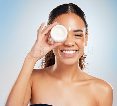 Buy stock photo Shot of a young woman applying cream to her face against a blue background