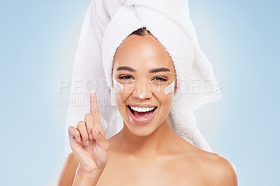 Buy stock photo Shot of a young woman applying cream to her face against a blue background
