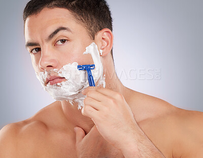 Buy stock photo Shot of a handsome young man shaving his facial hair