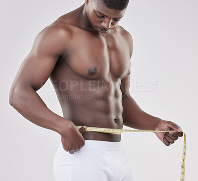 Buy stock photo Shot of a man measuring his waist using a measuring tape against a studio background