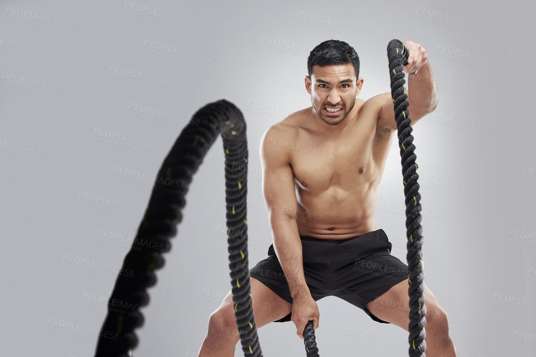 Buy stock photo Studio portrait of a muscular young man exercising with battle ropes against a grey background