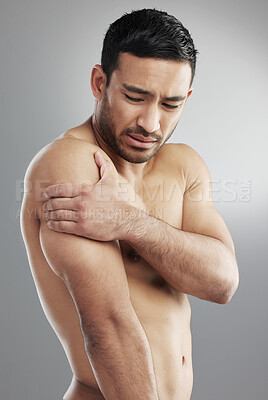 Buy stock photo Studio shot of a muscular young man experiencing shoulder pain against a grey background