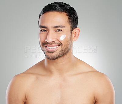 Buy stock photo Studio shot of a handsome young man applying moisturiser against a grey background