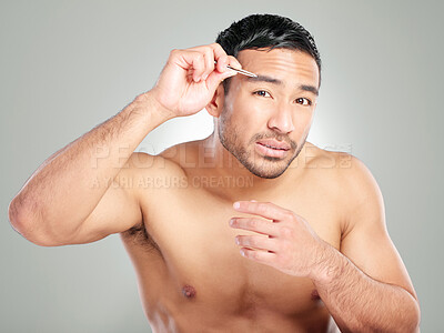 Buy stock photo Studio shot of a handsome young man plucking his eyebrows against a grey background