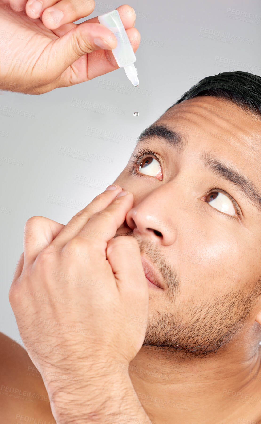 Buy stock photo Studio shot of a handsome young man applying eye drops against a grey background