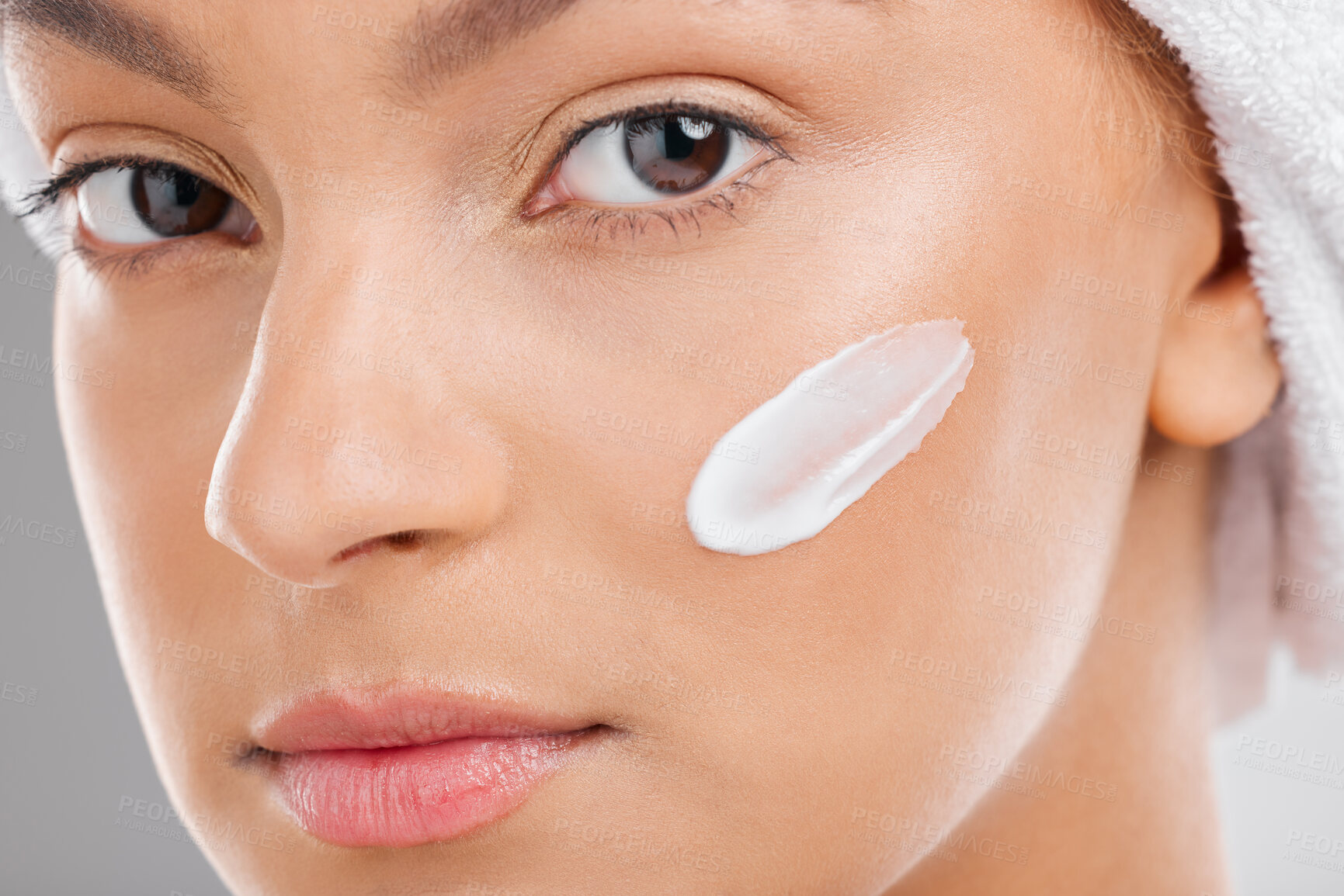 Buy stock photo Shot of an attractive young woman applying moisturiser to her face against a studio background