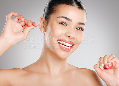 Buy stock photo Studio shot of an attractive young woman flossing her teeth against a grey background