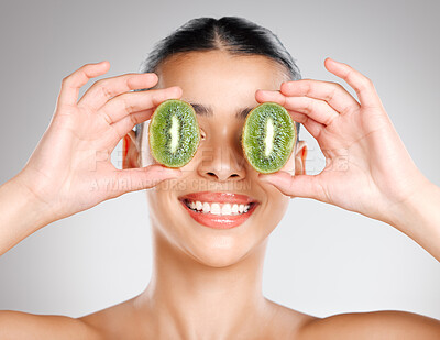 Buy stock photo Studio shot of an attractive young woman holding kiwi fruit to her face against a grey background
