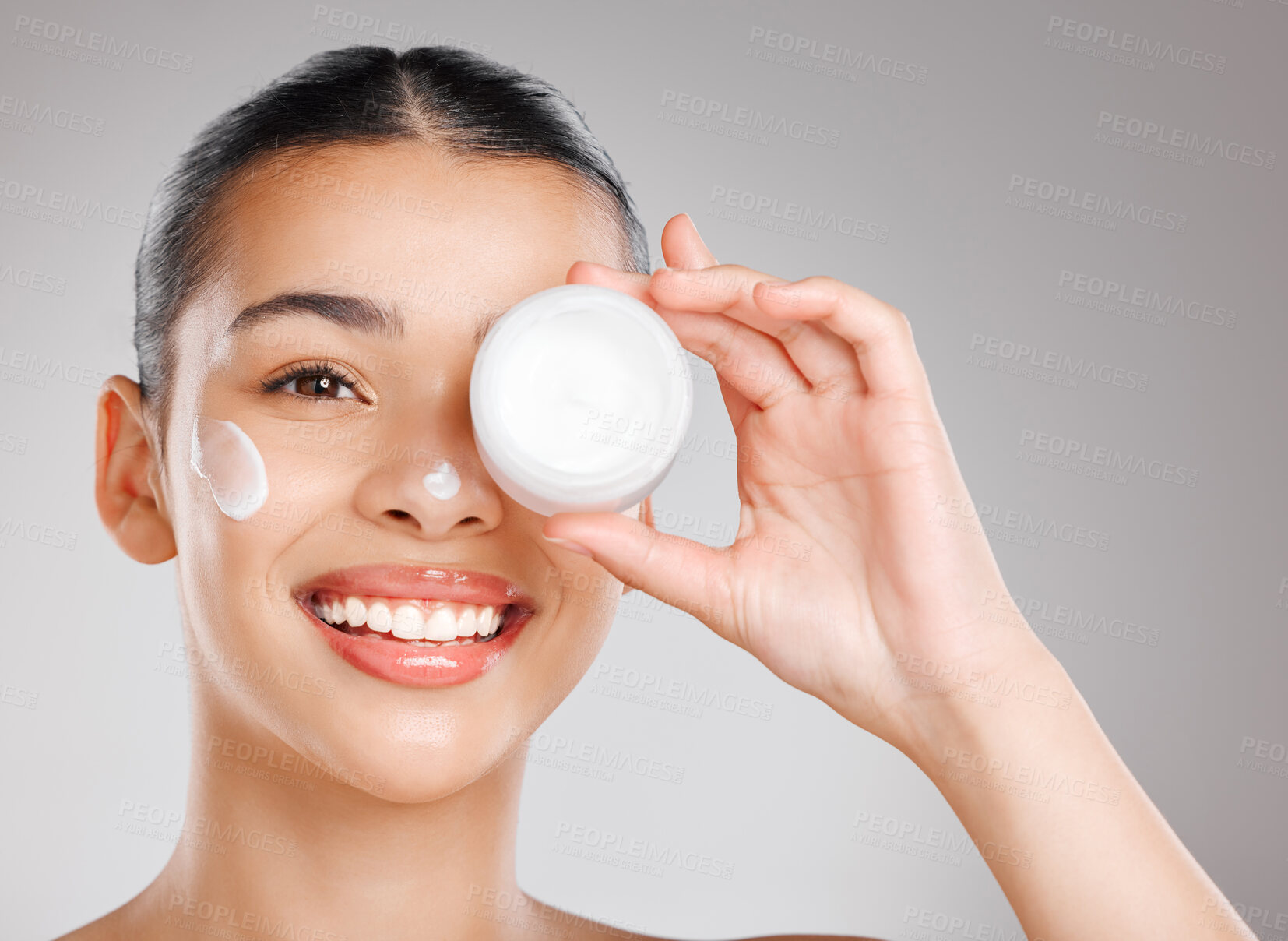 Buy stock photo Studio shot of an attractive young woman applying moisturiser to her face against a grey background