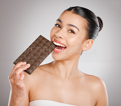 Buy stock photo Studio shot of an attractive young woman eating a slab of chocolate against a grey background