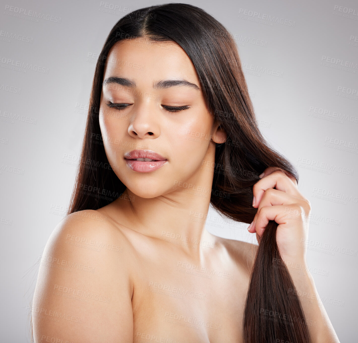 Buy stock photo Studio shot of an attractive young woman holding her hair against a grey background