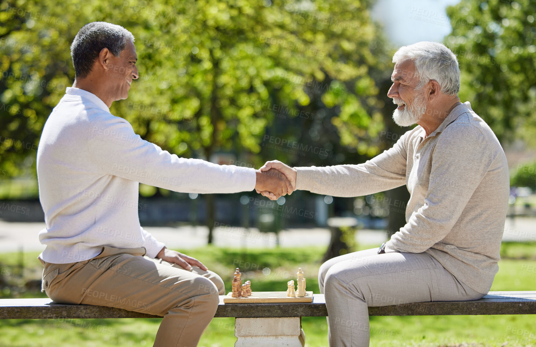 Buy stock photo Shot of two senior men sitting together on a bench in the park and shaking hands before playing chess