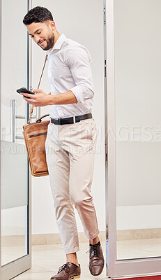 Buy stock photo Full length shot of a handsome young businessman checking his messages while walking into the office