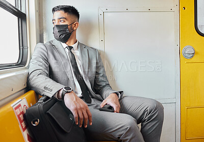 Buy stock photo Shot of a young businessman wearing a face mask while staring out the window on a train during his commute