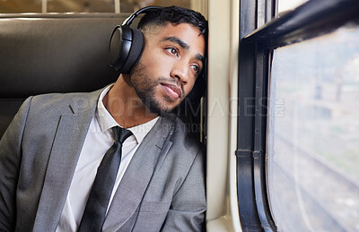 Buy stock photo Shot of a young businessman wearing headphones while staring out the window on a train during his commute