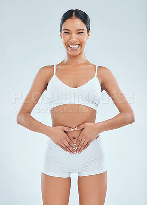 Buy stock photo Shot of an attractive young woman standing alone in the studio and posing with her hands over her belly