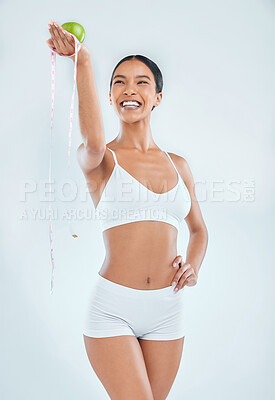 Buy stock photo Shot of an attractive young woman standing alone in the studio while holding an apple and measuring tape