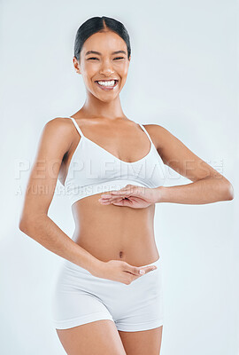 Buy stock photo Shot of an attractive young woman standing alone in the studio and posing with her hands around her belly