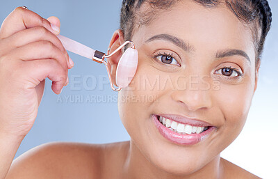 Buy stock photo Studio portrait of an attractive young woman using a jade roller on her face against a blue background