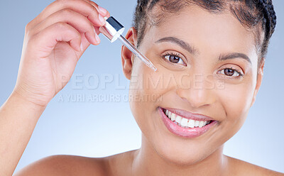 Buy stock photo Studio portrait of an attractive young woman applying serum to her face against a blue background