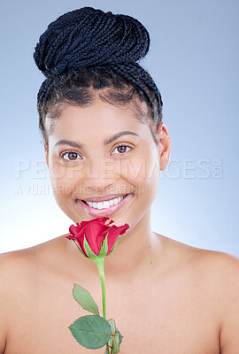 Buy stock photo Studio portrait of an attractive young woman holding a rose while posing against a blue background