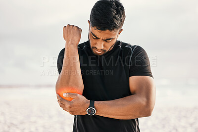 Buy stock photo Cropped shot of a handsome young male athlete holding his elbow in pain while exercising on the beach