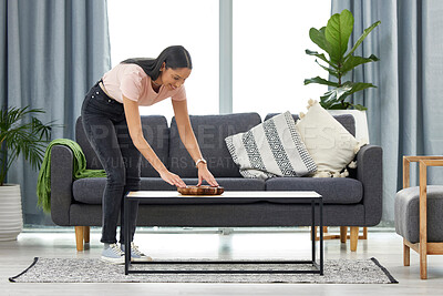 Buy stock photo Full length shot of an attractive young woman arranging her coffee table while cleaning at home