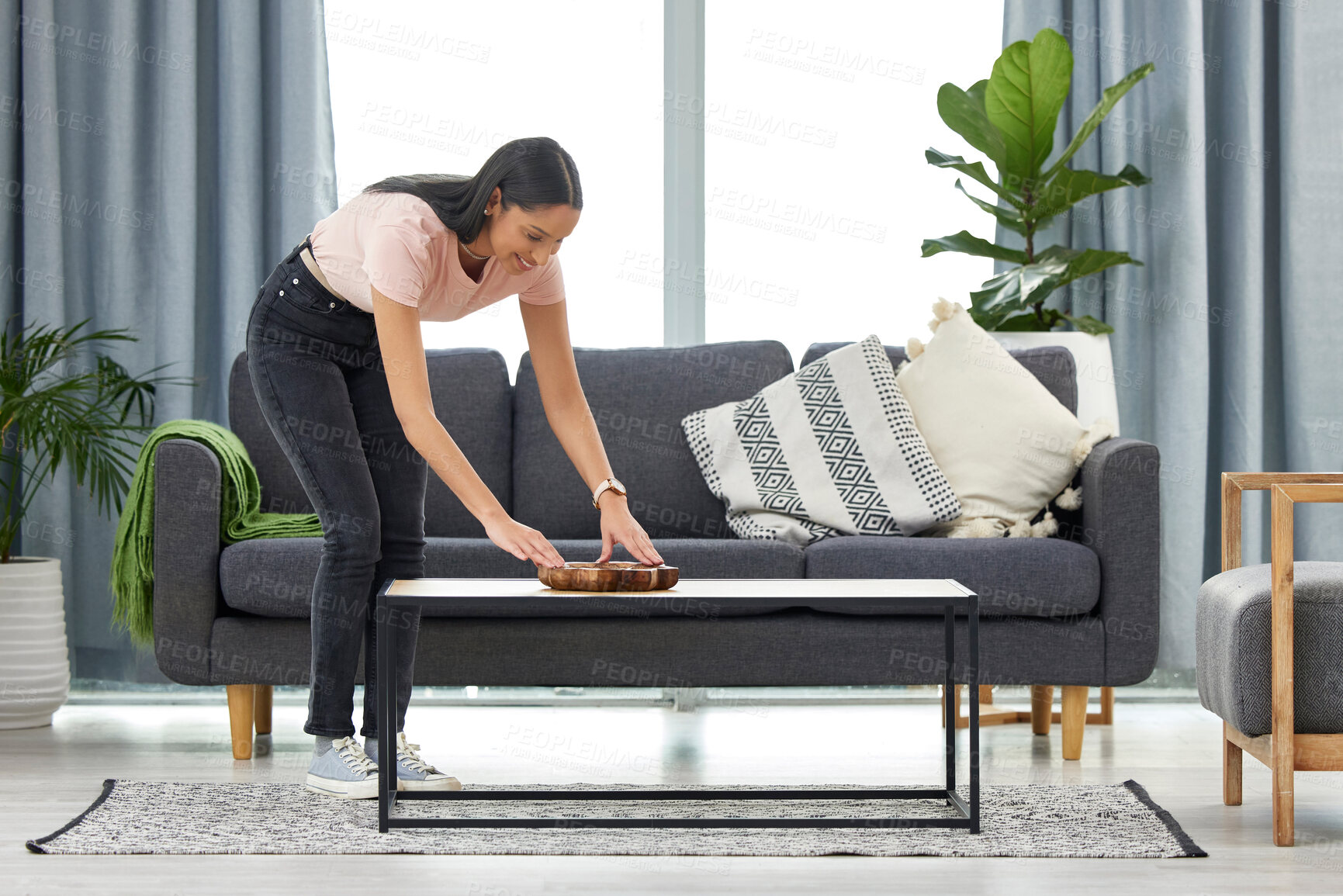 Buy stock photo Full length shot of an attractive young woman arranging her coffee table while cleaning at home