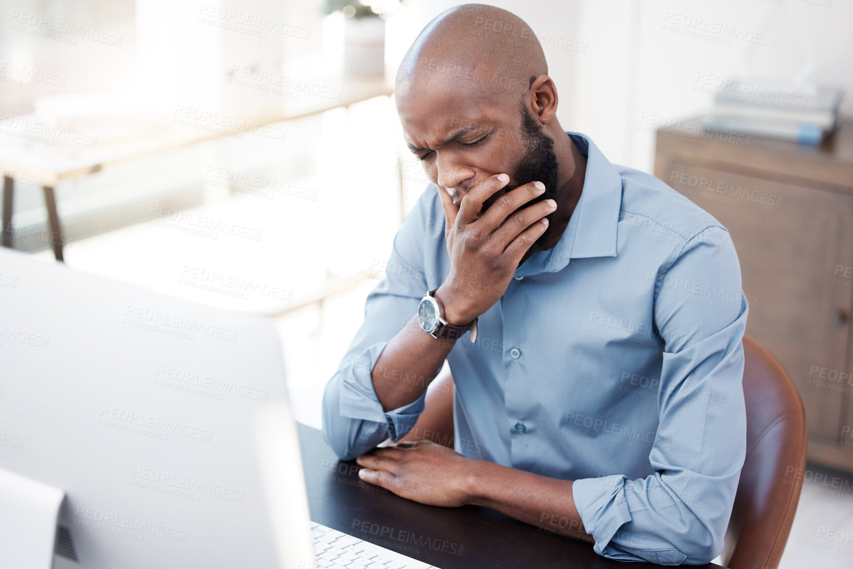 Buy stock photo Cropped shot of a handsome young businessman yawning while working on his computer in the office