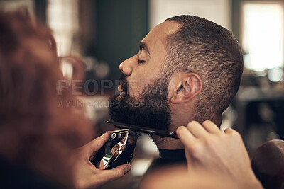 Buy stock photo Shot of a handsome young man sitting and getting his beard styled by his hairdresser