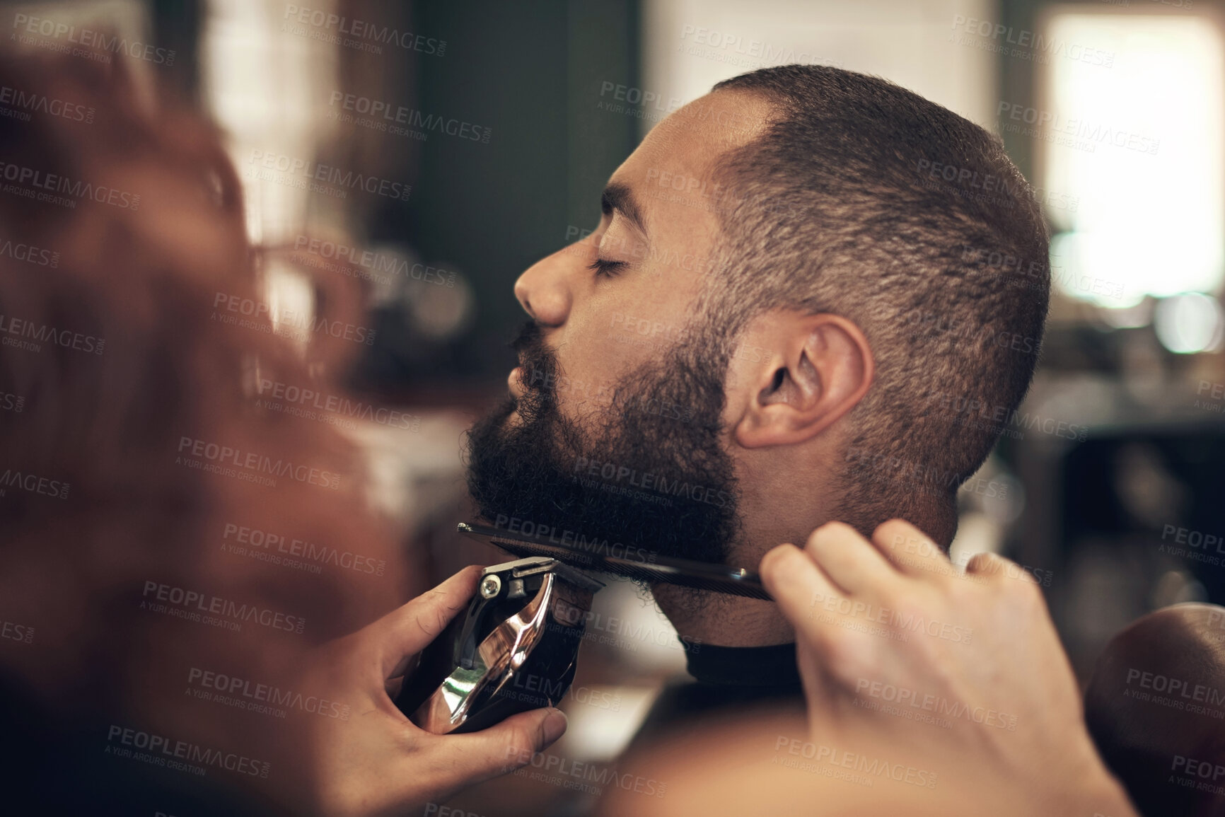 Buy stock photo Shot of a handsome young man sitting and getting his beard styled by his hairdresser