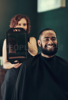 Buy stock photo Shot of a handsome young man sitting and admiring his hairstyle while his hairdresser hold the mirror