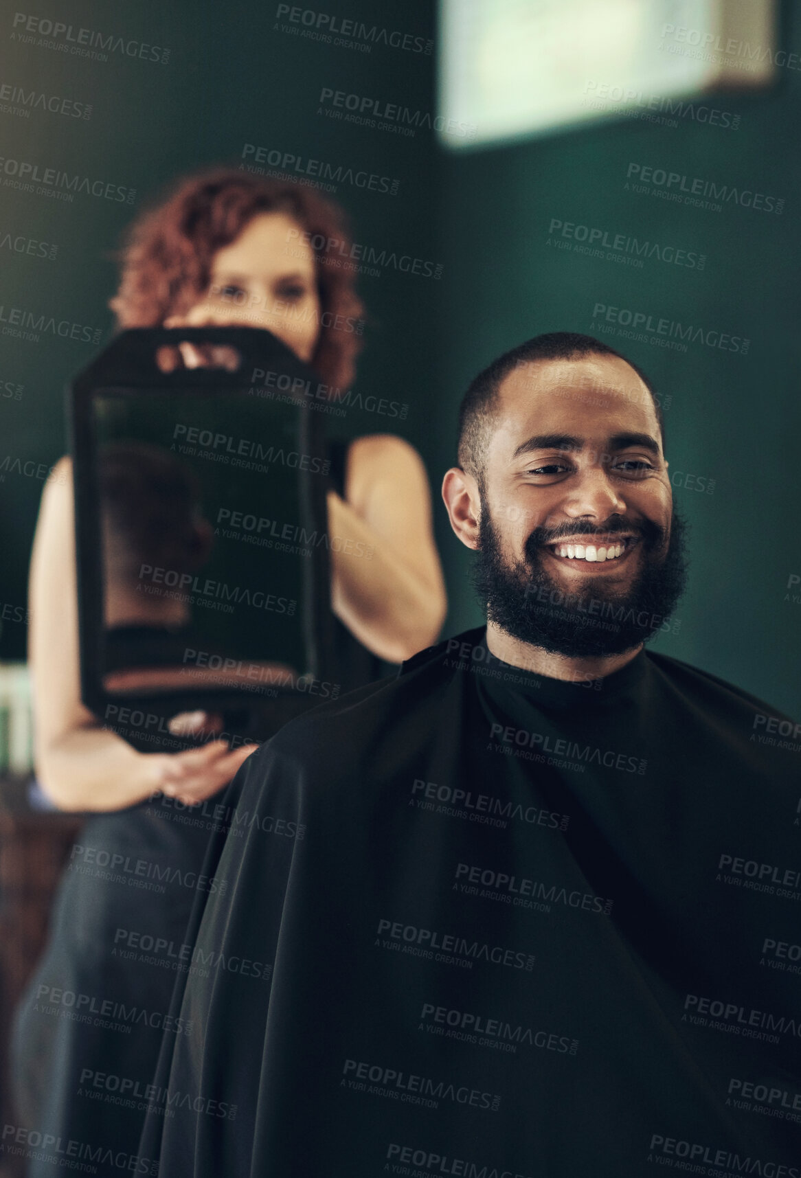 Buy stock photo Shot of a handsome young man sitting and admiring his hairstyle while his hairdresser hold the mirror