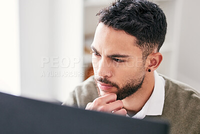 Buy stock photo Shot of a handsome young businessman sitting alone in the office and looking contemplative while using his computer