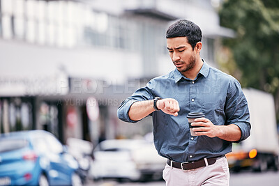 Buy stock photo Shot of a handsome young businessman checking his watch while walking through the city